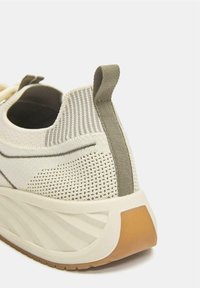 Lahka superga v kremni barvi z zgornjim delom iz teksturirane mreže, zelenimi poudarki in debelim gumijastim podplatom z vzorcem valov.