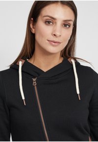 Felpa nera con zip, caratterizzata da una texture morbida, un cappuccio con lacci color crema e dettagli in bronzo sulla zip e nell'area delle spalle.