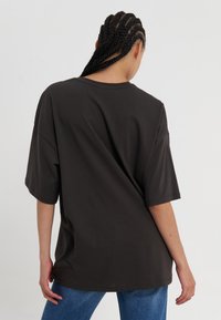 T-shirt noir oversize à manches courtes, fabriqué en coton doux. Design simple avec un col rond. Porté de manière décontractée avec du denim.