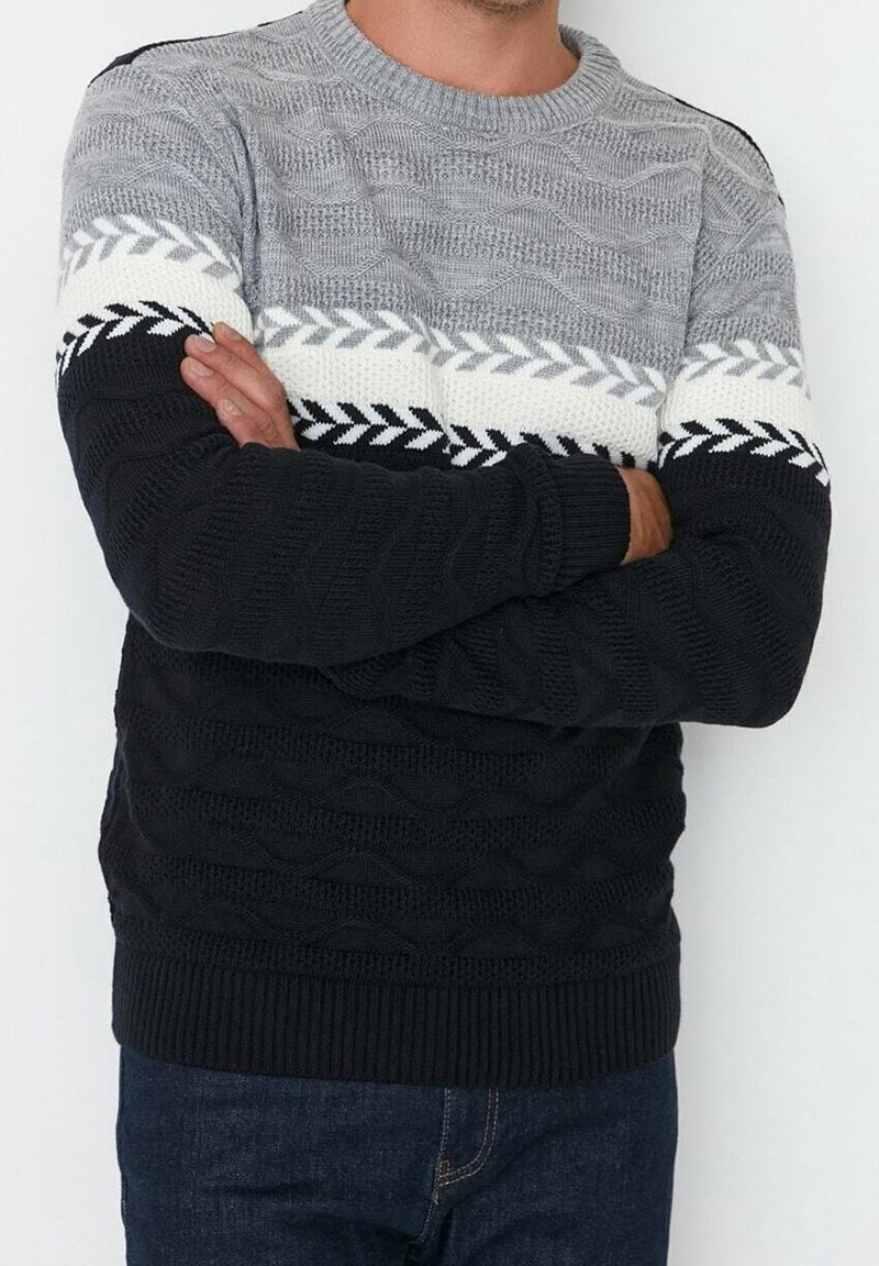 Pull en tricot avec un corps gris à texture ondulée, motifs blancs et noirs sur la poitrine, manches noires et bordure inférieure noire.