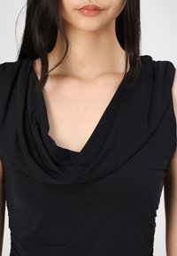 Zwarte mouwloze top met een gedrapeerde collet. Glad oppervlak, fitted ontwerp en plooien aan de zijkanten creëren een gestructureerde uitstraling.