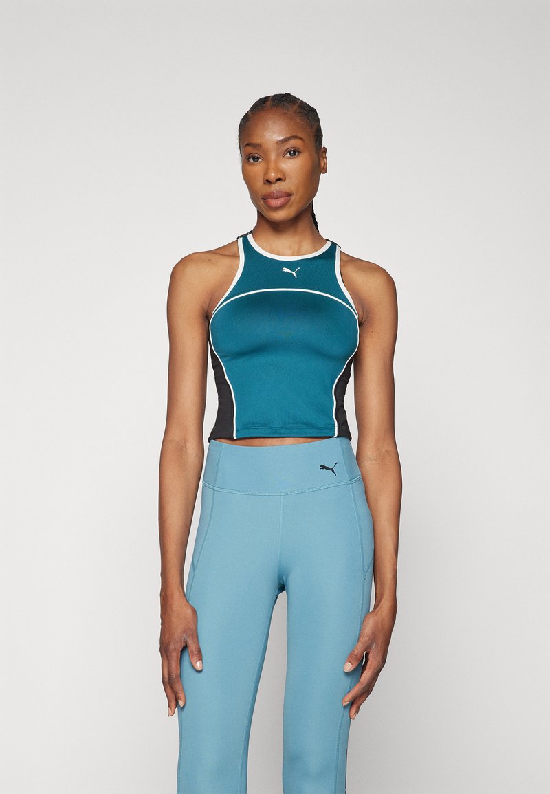 Zastrihnutý športový tank top v tealovej a čiernej farbe s bielymi akcentami, vyrobený z elastického materiálu. Kombinovaný s vysokými svetlomodrými legínami.