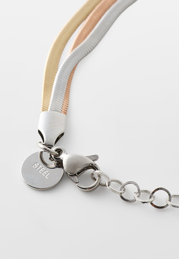 Wielokolorowy metalowy naszyjnik z trzema teksturowanymi pasmami w kolorze złotym, srebrnym i różowego złota. Posiada stalową zawieszkę i zapięcie na karabińczyk.