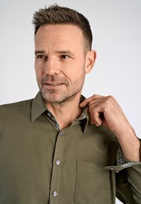Olijfgroen shirt met een gestructureerde pasvorm, voorzien van een gemêleerde binnenkraag en manchetten, knopen aan de voorkant en een borstzak. Geweven stof.