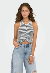 Top corto a righe, senza maniche, in bianco e nero con un dettaglio annodato davanti, abbinato a jeans strappati azzurri a vita alta.