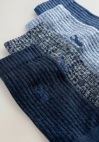 Three knitted socks in varying shades of blue, featuring ribbed texture and a subtle pattern, with a small embroidered logo on one sock.