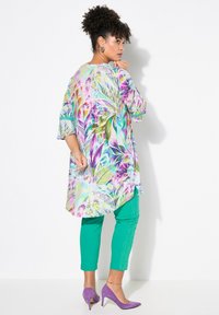 Mångfärgad tunika med palmbladsmönster, i kombination med gröna byxor i ankellängd och lila klackar. Slät tyg med lös passform.