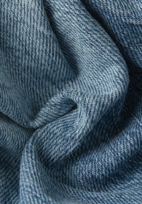 Tejido de denim en un tono azul claro con un tejido de sarga, que presenta una textura sutil y variaciones en el color a lo largo de su superficie.