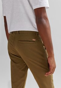 Olíva zöld pamut nadrág, slim fit szabással, hátsó zsebekkel és márkás címkével. Fehér, rövid ujjú inggel párosítva.