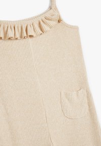 Beige ribbed Stofftop mit einem rüschenartigen Ausschnitt und einer kleinen Tasche. Die Textur wirkt weich und hat durchgehende vertikale Streifen im Kleidungsstück.