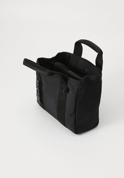 Sac fourre-tout noir en tissu avec deux poignées supérieures, poche zippée intérieure et détail en relief sur le côté. Forme rectangulaire avec un design minimaliste.