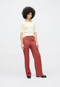 Svetlo rumena oprijeta majica s tremi četrtinami rokavi, združena s širokimi rdečimi hlačami z vzorcem črnih in bež diamantov.