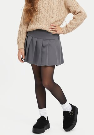 Gray pleated skirt paired with a beige cable-knit sweater. Model wears black platform shoes and white ankle socks, complemented by sheer tights.