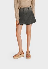 Maglione lavorato a maglia beige abbinato a una gonna di jeans nera e sandali con zeppa color cammello, caratterizzati da una base intrecciata e una fibbia decorativa sulla cinghia.