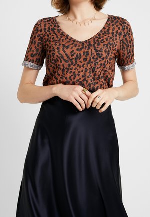 Femme portant un haut à manches courtes imprimé léopard et une jupe en satin noire, avec un collier en or et une bague en or à la main gauche.