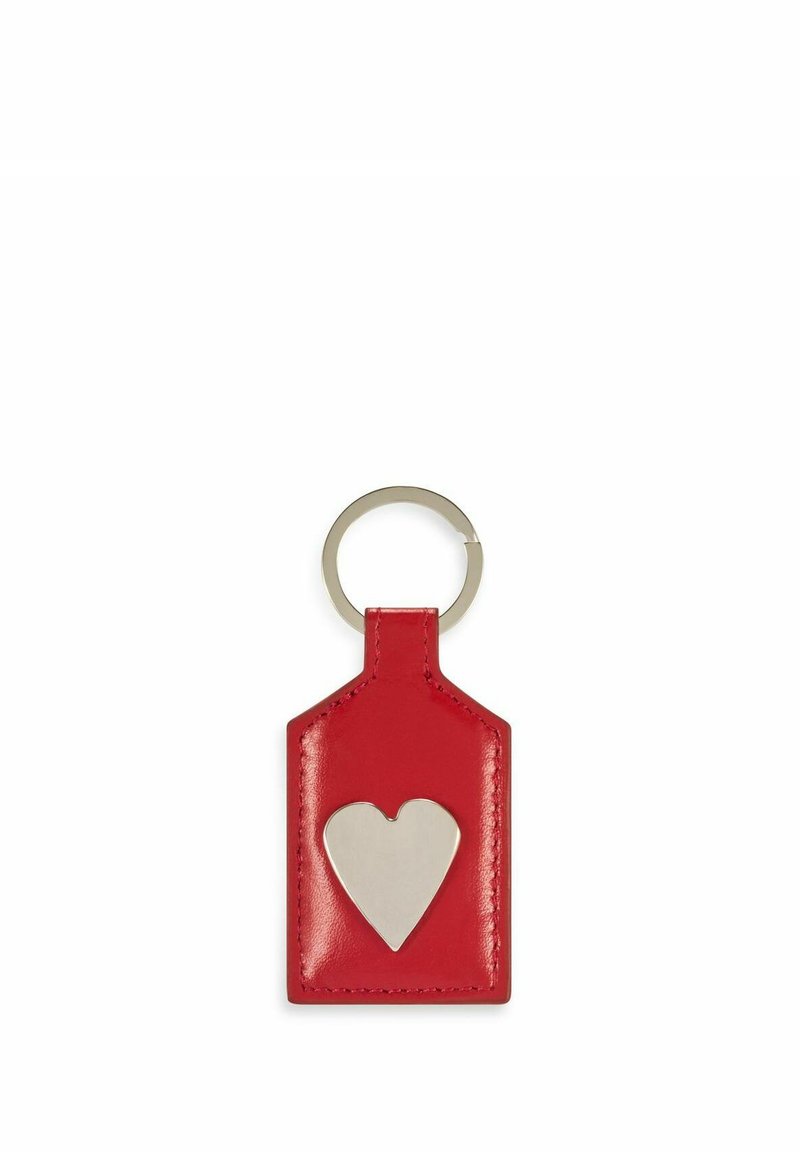 Czerwony skórzany brelok w kształcie metki z wyciętym srebrnym sercem, wyposażony w metalowy pierścień do przypięcia. Gładka tekstura.