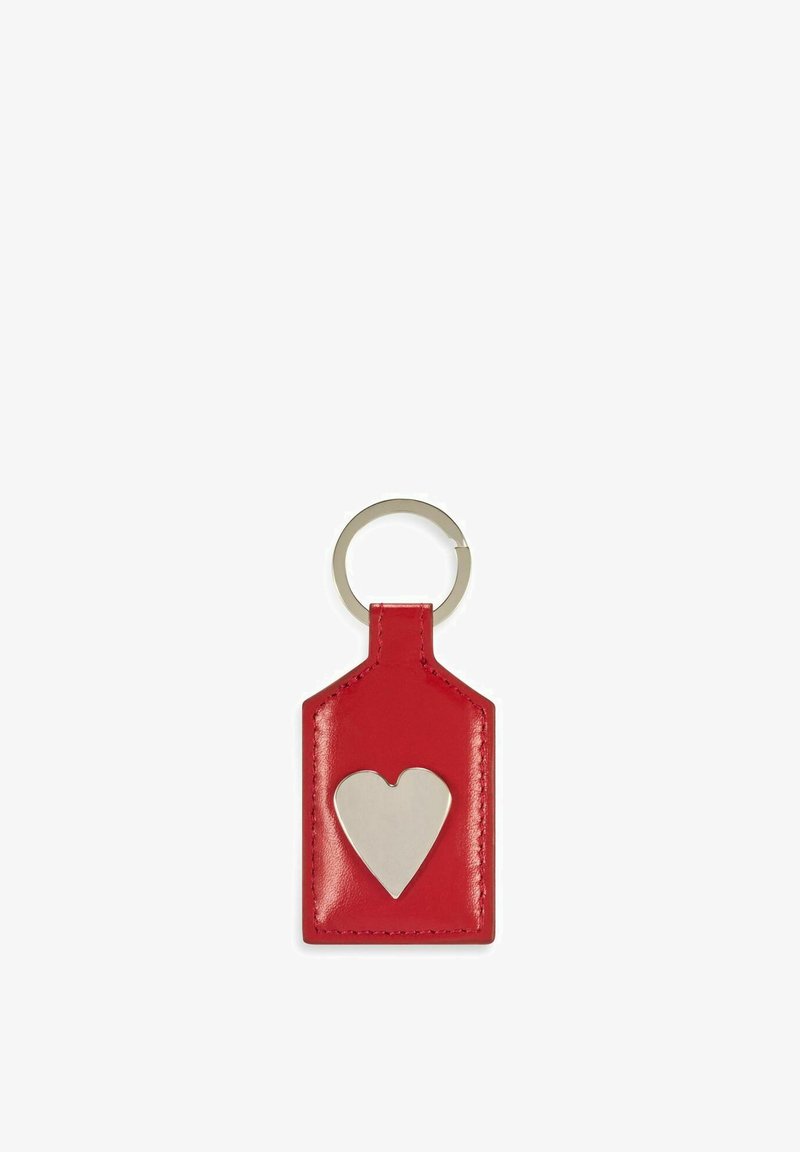 Czerwony skórzany brelok w kształcie metki z wyciętym srebrnym sercem, wyposażony w metalowy pierścień do przypięcia. Gładka tekstura.
