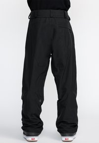 Pantalons de neige noirs avec une coupe droite, fabriqués en matériau léger. Comprend une poche arrière et un détail de logo subtil près de l'ourlet.