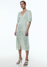 Floral midi Kleid in Hellblau mit Puffärmeln, V-Ausschnitt, einem Schlitz vorne und kleinen gelben und grünen Blumen überall.