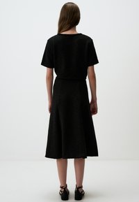 Zwarte jurk met korte mouwen en een uitlopende rok. Gestructureerde stof, knie-lengte, relaxte pasvorm en een ronde halslijn. Gekocht met zwarte sandalen met bandjes.
