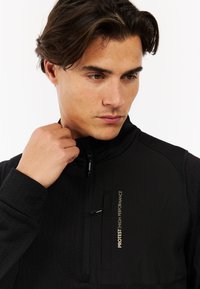 Zwarte half-zip pullover van textuurstof, met een ritszak aan de voorkant en subtiele gouden branding op de borst.