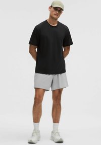 Camiseta negra, pantalones cortos grises y calzado ligero con acentos blancos. Diseño sencillo, mangas cortas y corte relajado. Una gorra ligera completa el look.