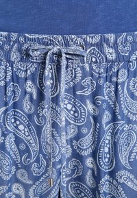 Shorts à taille élastique bleue avec un motif paisley blanc, dotés d'un cordon de serrage avec embouts en métal. Tissu doux, design décontracté et surface texturée.