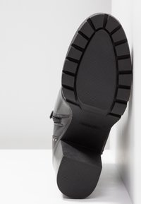 Botte de cheville en cuir noir avec une semelle en caoutchouc texturée, un bout arrondi et des clous décoratifs sur le côté, dotée d'une fermeture éclair.