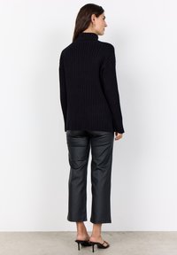 Schwarzer gerippter Rollkragenpullover mit langen Ärmeln, kombiniert mit schlanken schwarzen Kunstlederhosen, von hinten betrachtet.