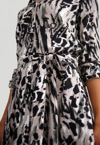 Button-up dress featuring a black, white, and gray abstract pattern, a tied waist belt, and rolled sleeves with a smooth fabric texture.