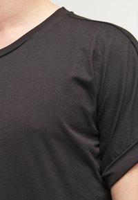 Camiseta de algodón negra con cuello redondo, mangas ajustadas y textura suave. Cuenta con un sutil detalle de costura en los hombros.
