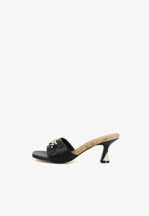 Mule nero con punta aperta, tacco largo di media altezza e emblema decorativo dorato sulla larga fascia in pelle.