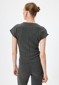 Strukturierte schwarze Bluse mit kurzen Ärmeln, die eine figurbetonte Passform und ein dezentes, gewelltes Muster aufweist, von hinten betrachtet.