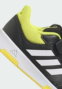 Zapatilla deportiva negra y amarilla con parte superior sintética texturizada, acentos de malla, marca blanca y una suela de goma resistente.