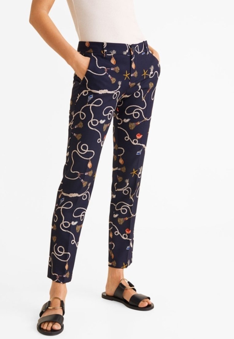 Pantalon bleu marine à motifs, comprenant des dessins floraux, des lignes entrelacées et des poches, confectionné dans un tissu lisse. Porté avec des sandales noires.