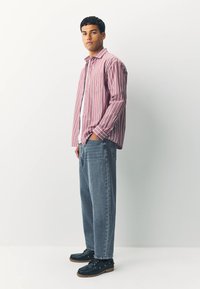 Punaste ja valgete triipudega nööpidega särk, hallid teksapüksid ja tumesinised paeltega jalanõud. Särgil on rinnatasku; pükstel on lõdvestunud istuvus.