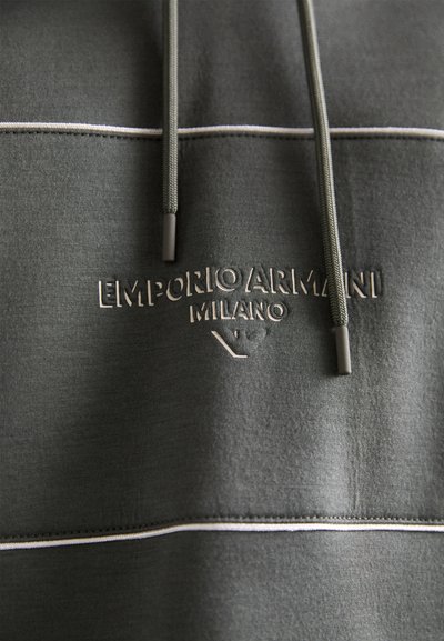 Hanorac gri cu o suprafață texturată, dungi orizontale albe și un logo embosat „EMPORIO ARMANI MILANO” cu șnururi ajustabile.