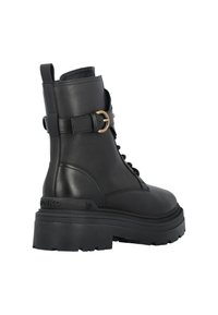 Stivale alla caviglia in pelle nera con una spessa suola platform, parte anteriore con lacci e una fibbia decorativa dorata di lato. Texture liscia, design robusto.