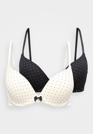 To polkadot-BHer som overlapper hverandre, en hvit med svarte prikker og sløyfe, en svart med hvite prikker, begge med tynne justerbare stropper.