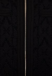 Zwarte zip-up trui met gestructureerde patronen, voorzien van geribbelde delen en een centrale zilveren rits, gemaakt van gebreide stof.