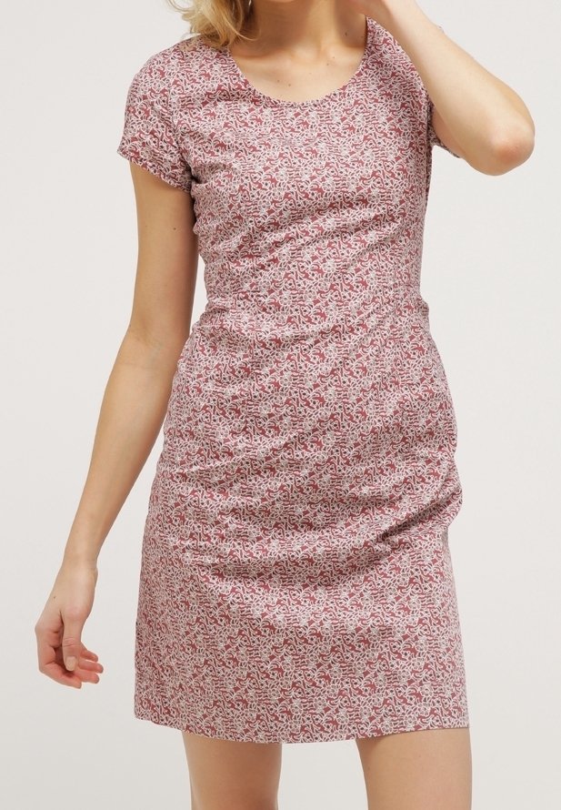 Femme portant une robe ajustée à manches courtes, longueur genou, avec un motif floral rouge et blanc sur fond clair.