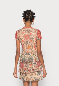 Robe aux motifs multiples mélangeant rouge, bleu et beige. Manches courtes, corsage ajusté et jupe à volants superposés.