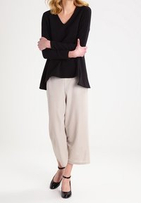 Top nero a maniche lunghe con scollatura a V e vestibilità comoda, abbinato a pantaloni beige a palazzo e décolleté neri in pelle lucida con cinturini alla caviglia.
