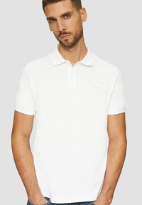 Weißes Poloshirt aus Baumwolle mit klassischem Kragen, kurzen Ärmeln und dezentem Logo auf der Brust. Nahtloses Design.