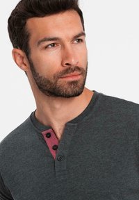 Mörkgrå henley-tröja med en vinröd accentplacket och tre knappar, med korta ärmar och rundad halsringning.