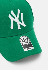 Căciulă de baseball verde cu logo-ul brodat alb al echipei New York Yankees, având un material texturat și o curea ajustabilă. Include un etichetă a mărcii.