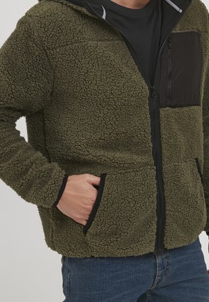 Olijfgroen fleece jack met een gestructureerde stof, rits aan de voorkant en een zwarte borstzak. Voorzien van zijzakken en zwarte accenten.