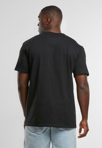 Black cotton t-shirt with short sleeves, a crew neck, and a relaxed fit, paired with light blue denim jeans. Textured fabric, simple design.