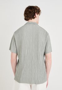 Camisetta a maniche corte di colore verde chiaro con strisce verticali a trama, colletto a rivolto e vestibilità morbida. Il tessuto sembra sottile e traspirante.