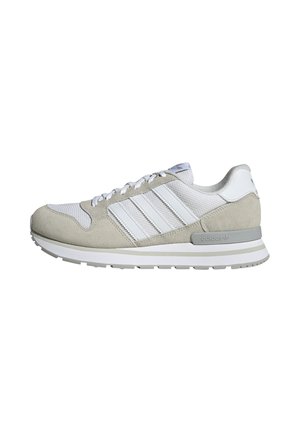 Zapatilla Adidas de perfil bajo en blanco y gris claro con paneles de malla y ante, tres franjas laterales blancas y suela acolchada.